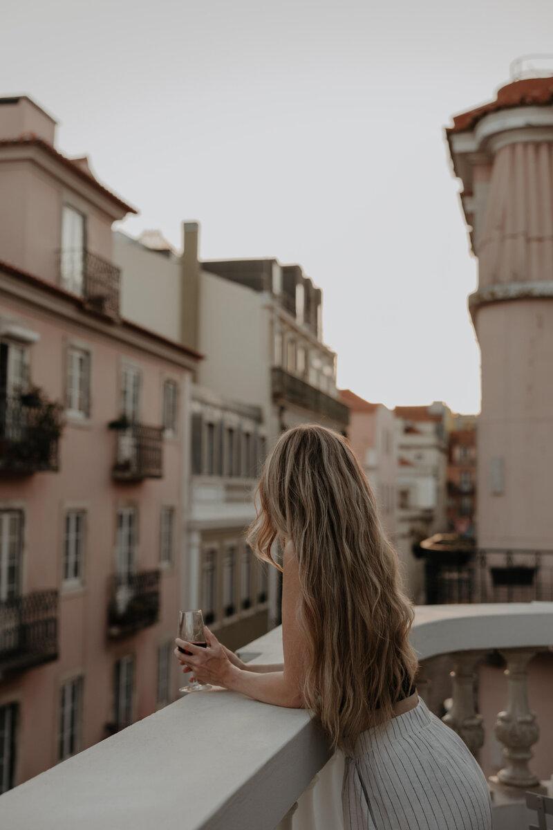 summer leigha photo sitting on a balcony in lisbon, portugal drinking a glass of wine while looking at the city views