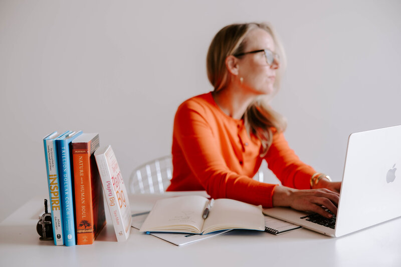 Heather Frick executive coach in a red sweater typing on a laptop surrounded by books
