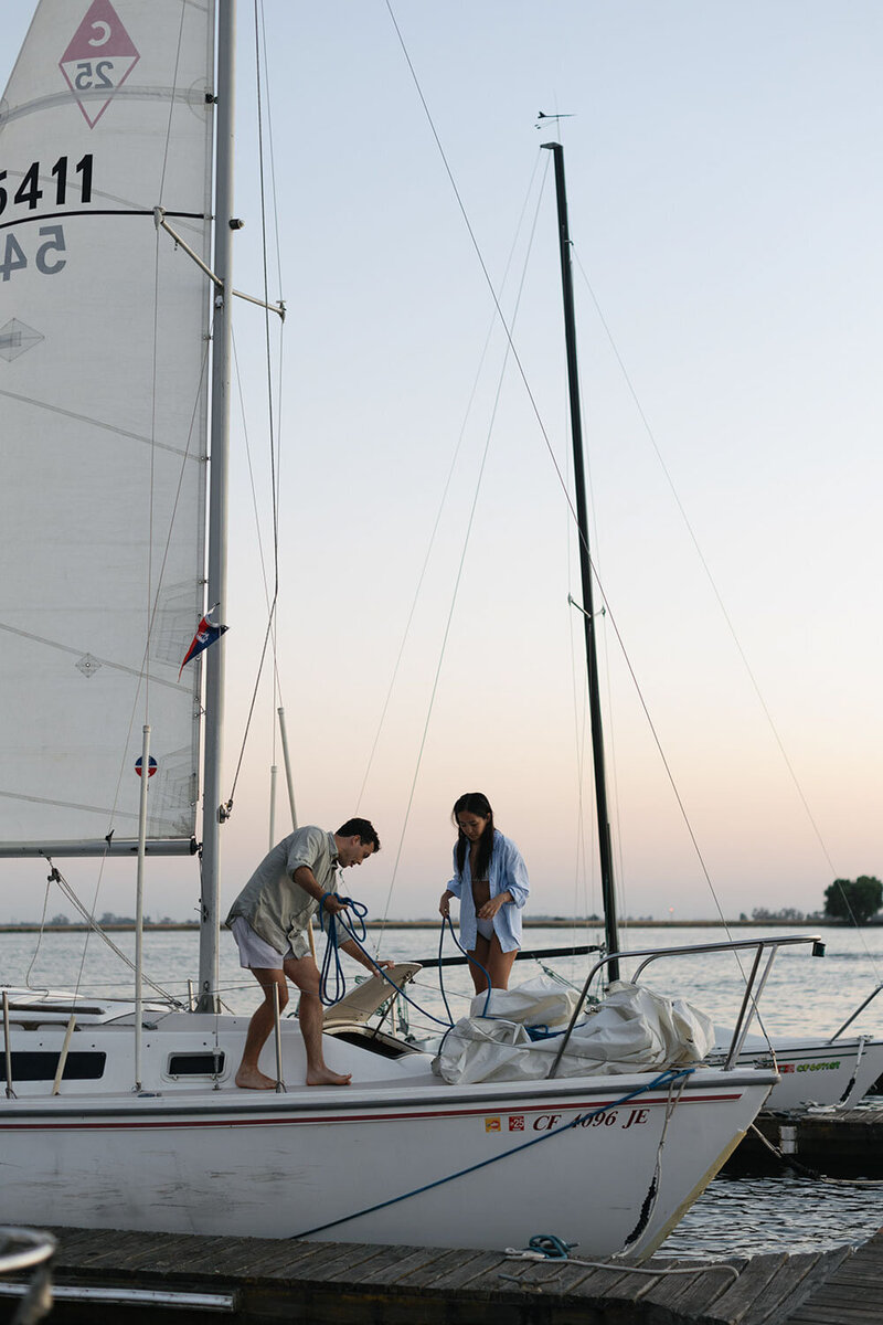 A man and woman on a sailboat at a dock.