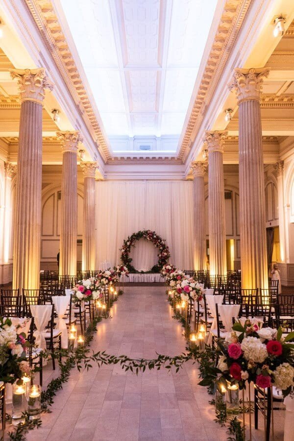 A wedding aisle lined with tea lights and pink flowers that leads to a wreath