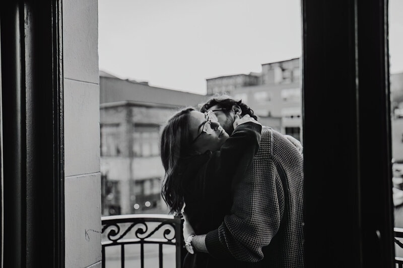a couple in a hug on a landing with buildings surrounding them. 