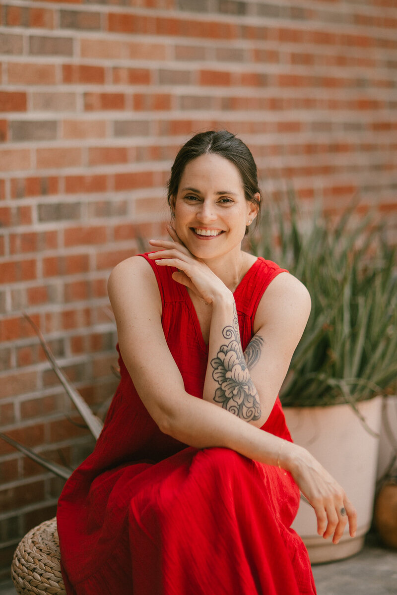 A woman sitting down and smiling at the camera in front of potted plants