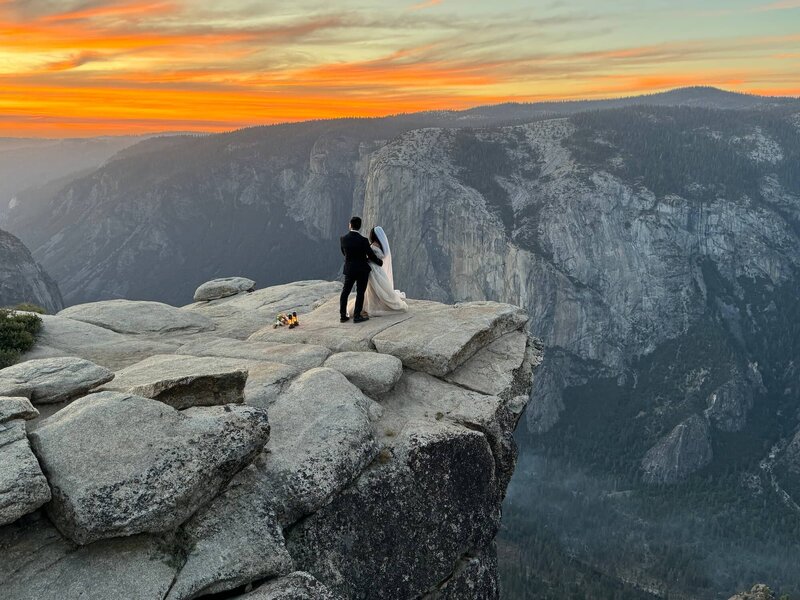 Bride and groom stand on cliff edge during sunset elopement at Taft Point, Yosemite