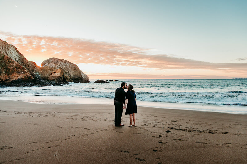 Couple standing on the beach at sunset with the cliffs of San Francisco's Baker Beach in the background, captured by San Francisco elopement photographer Kristin Smith.