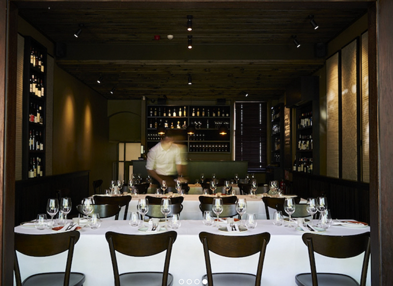 A barman working behind the bar at a wine bar with restaurant tables