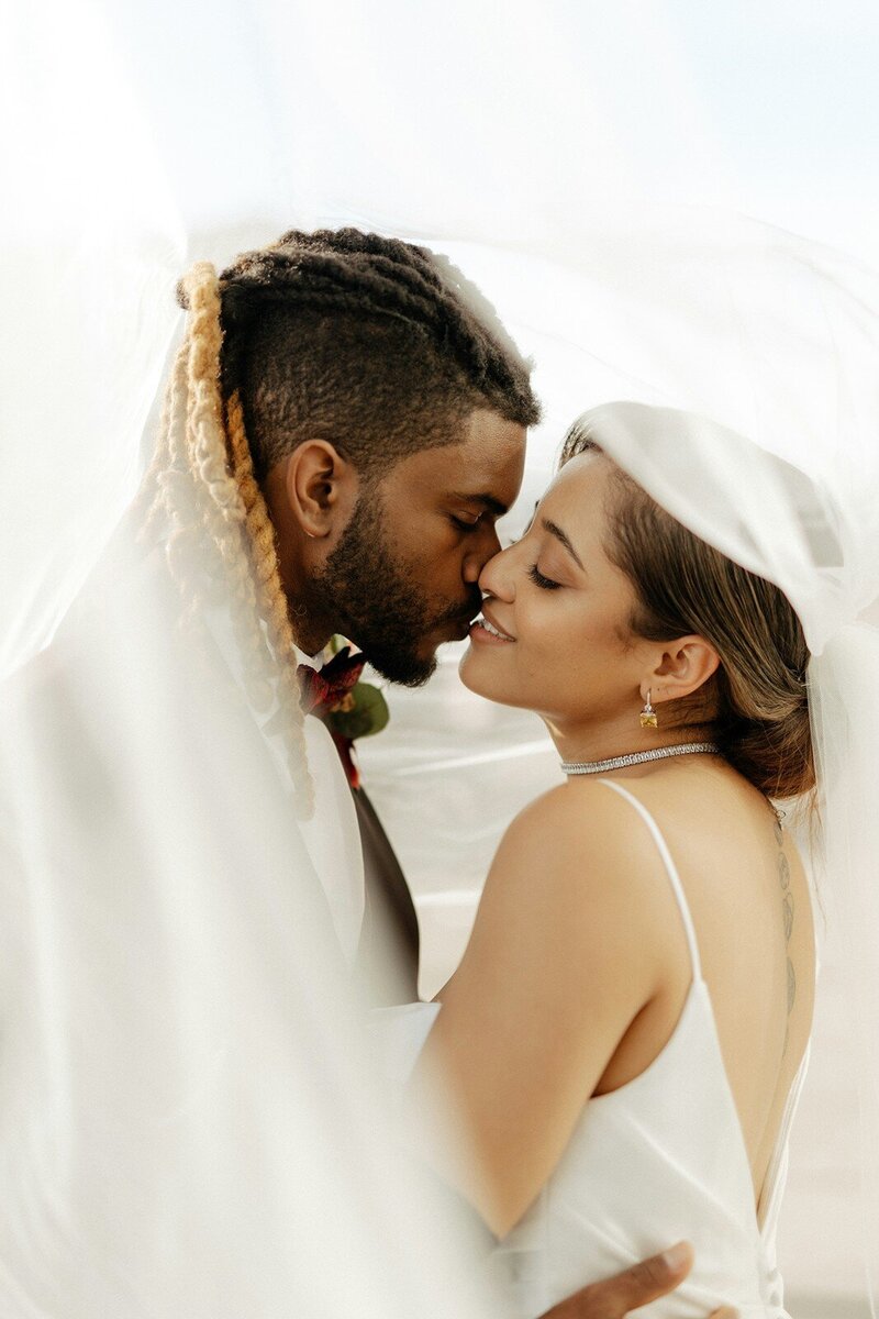 Bride and groom sharing a kiss under a flowing veil