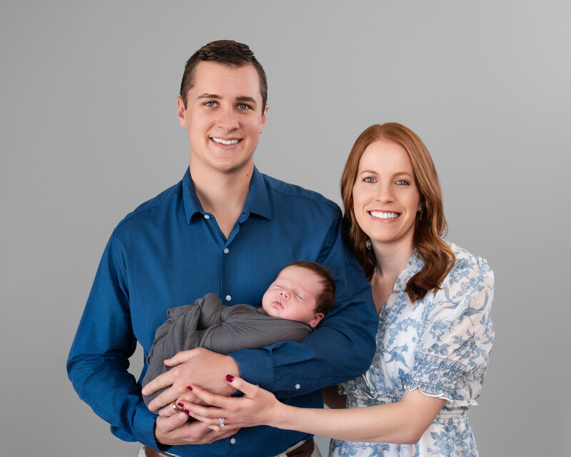 Two young parents smile for the professional photographer while holding their newborn boy