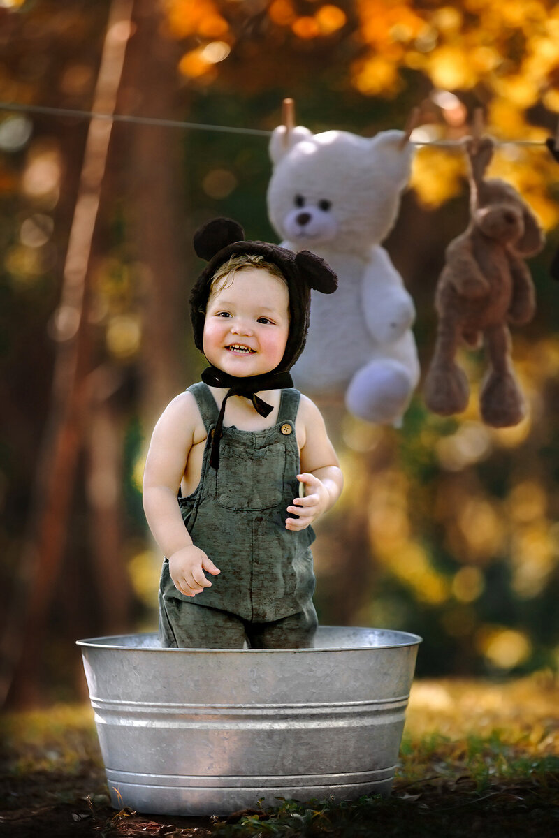 Happy little boy wearing a bear bonnet standing inside a metal tub outside in Houston, TX.