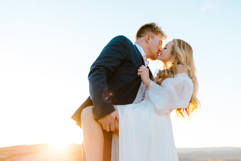 Bride and groom kissing and leaning over at golden hour