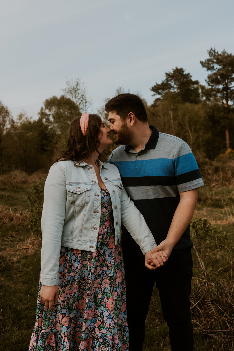 An adventurous couple embraces in the midst of a breathtaking natural landscape, sharing a gentle kiss in the evening sun