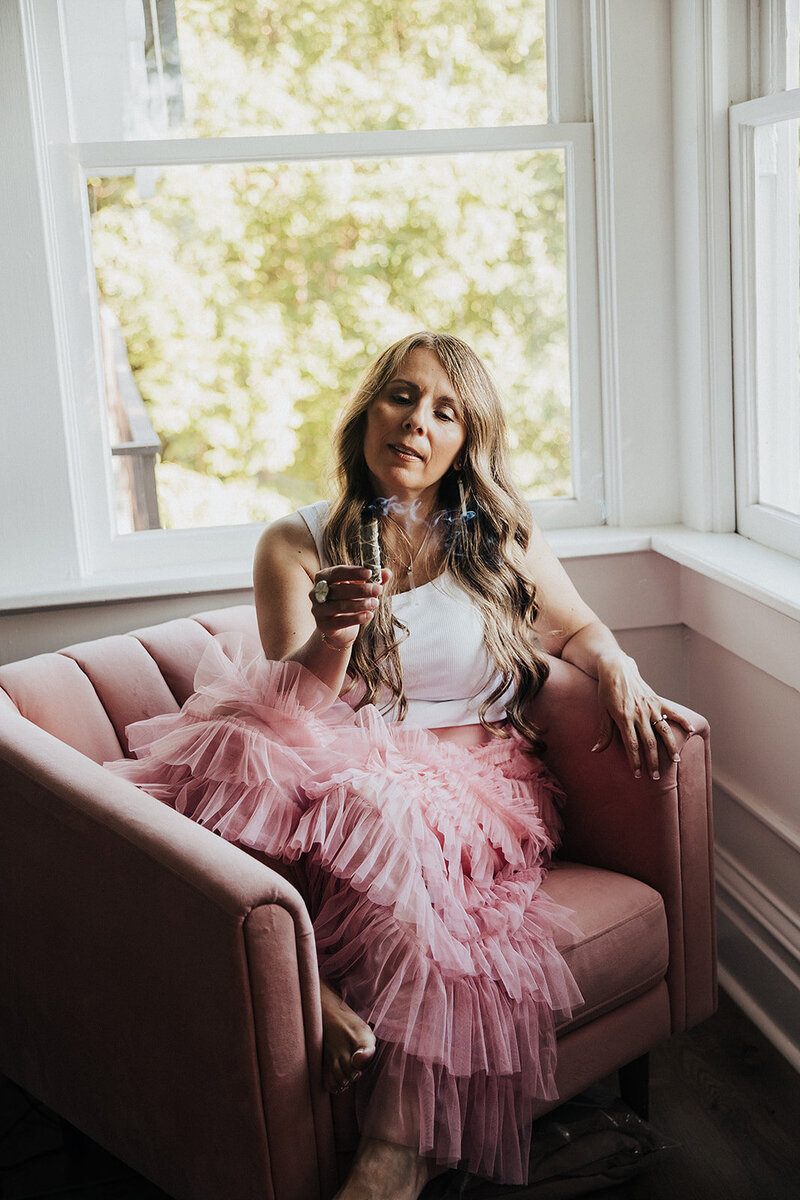 Patty sitting in a chair in a pink skirt with a smudge stick 