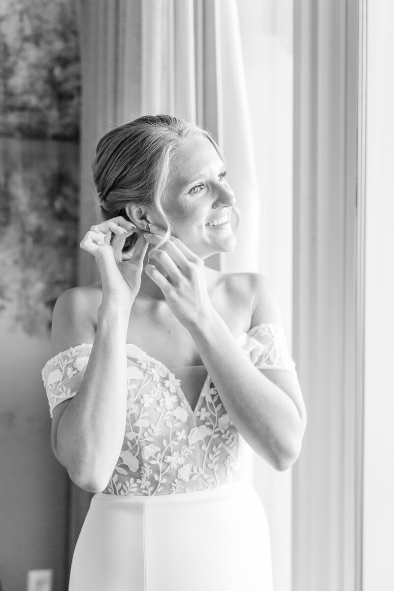 Black and white image of bride putting in earring at window Bride and Groom dip kiss in front of Marriott Grand National | Opelika Wedding Photographer Amanda Horne
