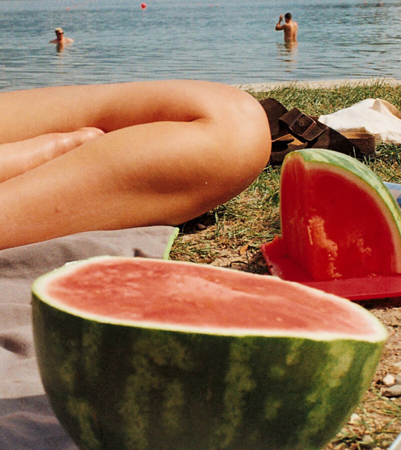 Nostalgic beach picnic with a halved watermelon and people swimming