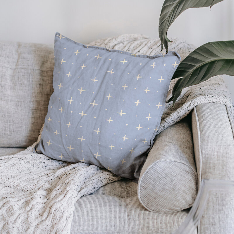 hand drawn twinkle stars in cream against a calming sky blue background adorn this playful simple print - shown on a linen pillow on a cozy couch