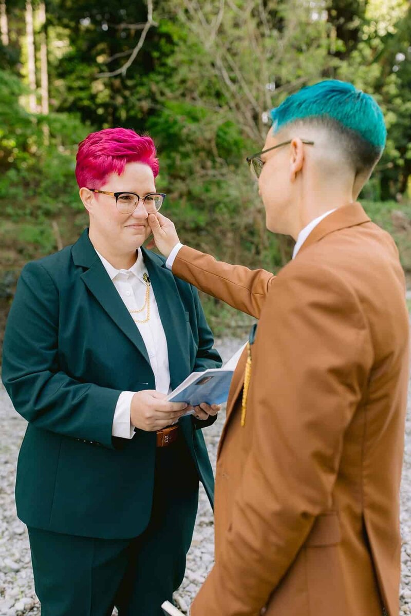 Two brides in suits looking at each other during their wedding ceremony. 