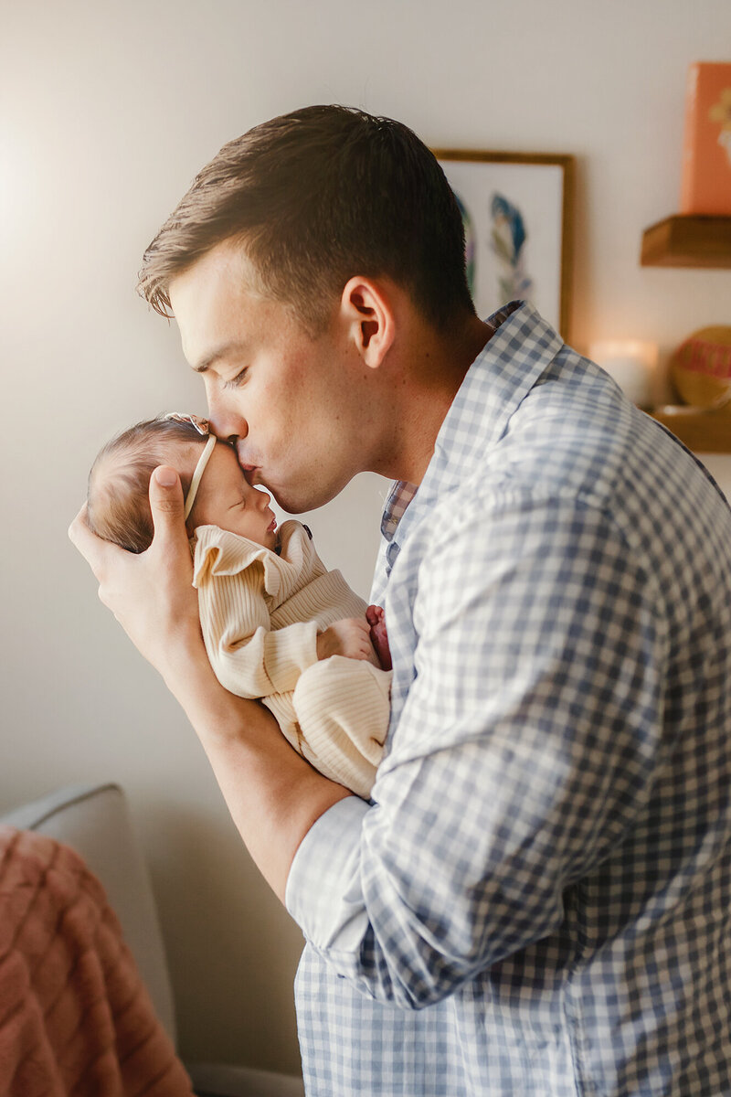 New father kissing his newborn daughter on the forehead