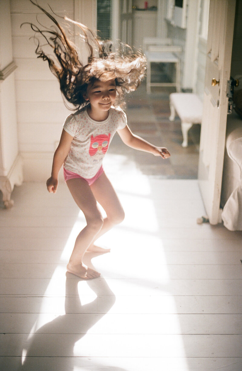 Child dancing in the hallway with sunlight streaming in, a sweet moment from a family photoshoot in Sydney by Tealily