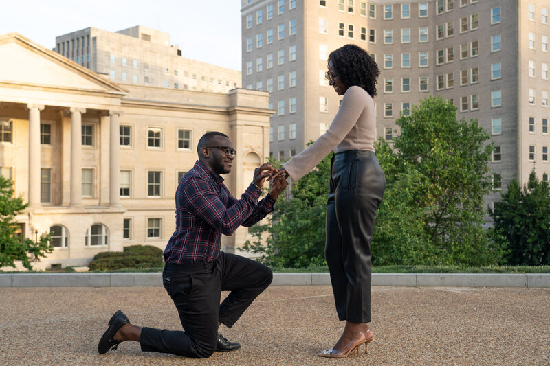 A man in a plaid shirt surprises his girlfriend with a ring as he proposes to her in Richmond, Virginia.