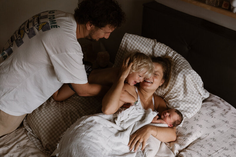 knuffelen in bed in de kraamweek. Moeder, vader, grote broer en baby.