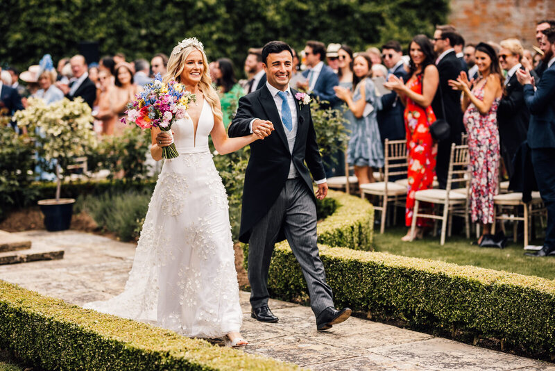 Bride and groom walk back down aisle after ceremony is completed in garden