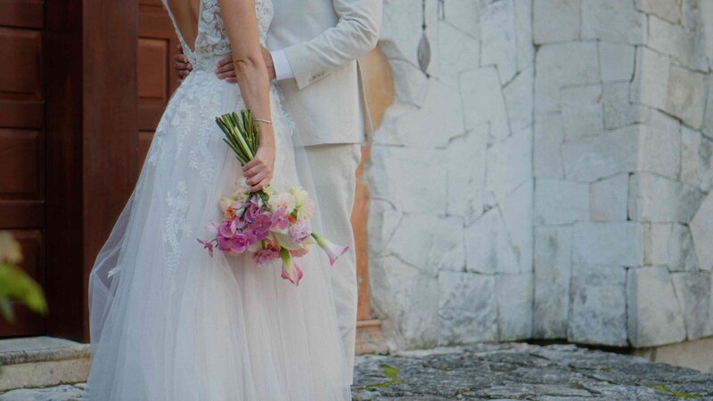 Close-up of a wedding bouquet with a couple’s hands embracing it.