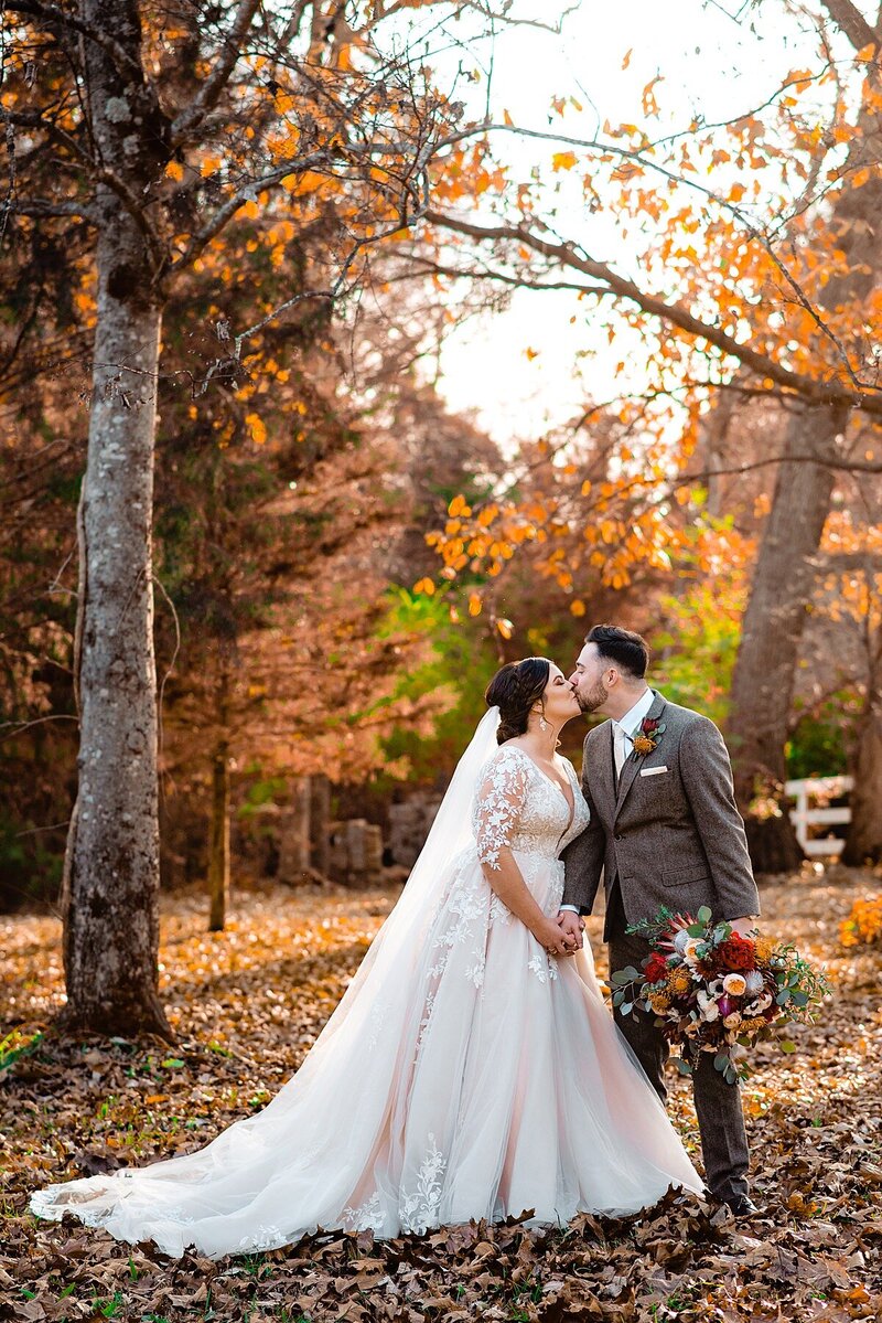 Couple leaning in to share a kiss under the fall foliage
