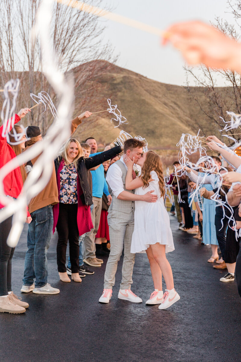 A couples kiss among streamers with Butte Mountains behind them.