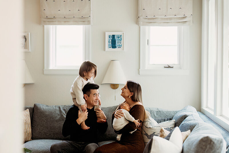 Family of four enjoying each other's company in the bright white living room for an at home newborn photo session in Denver