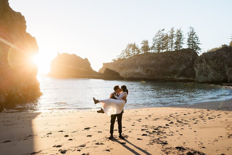 A groom picks up the bride and kisses her on the beach in northern California.