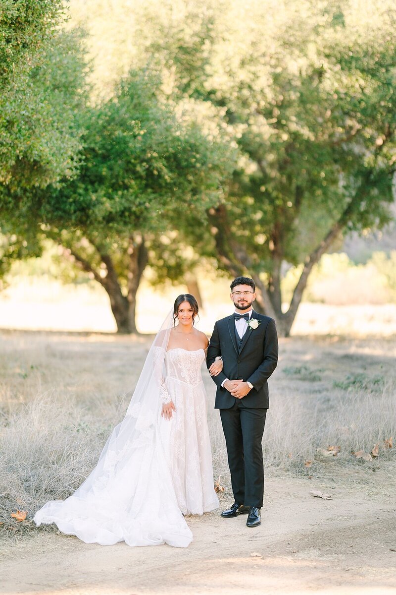 Bride and groom standing together under oak trees at Rancho Guejito Weddings Vineyard in Escondido, California.