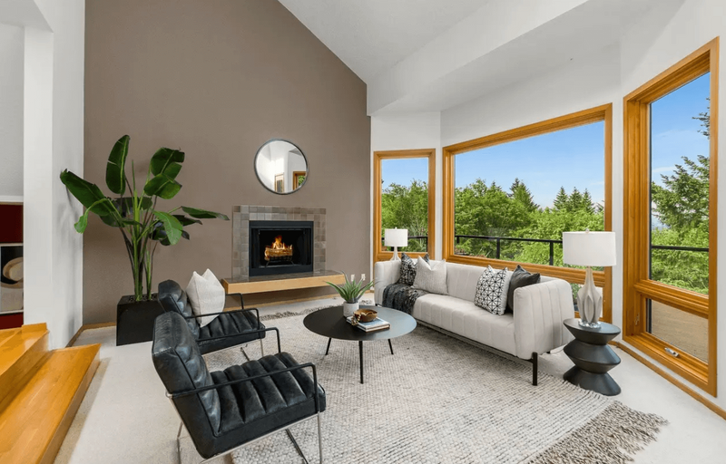 A living room featuring a fireplace, black chairs and a couch in front of large windows.