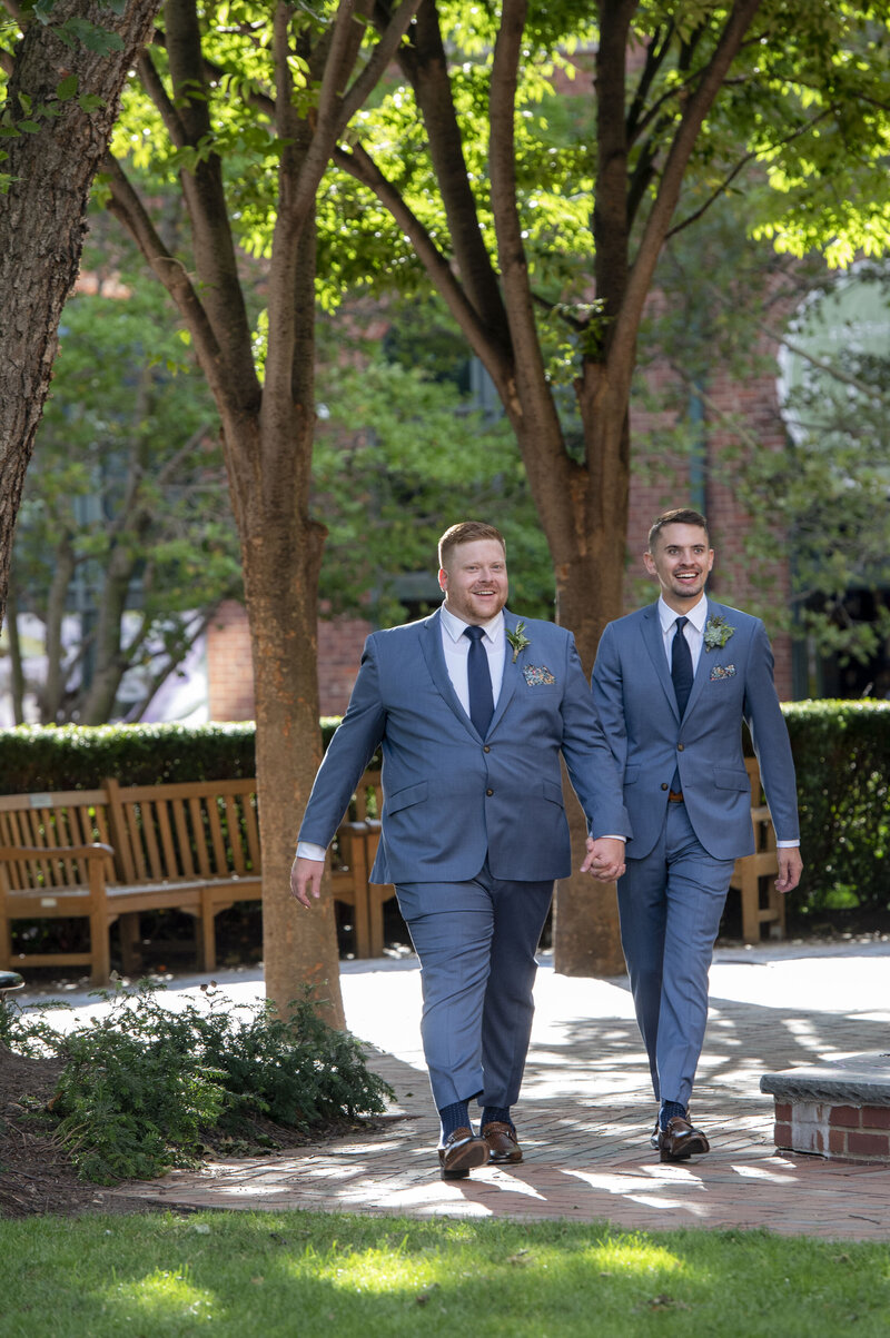 A newlywed couple in suits holding hands and walking together 