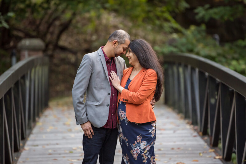 A husband and pregnant wife standing on a bridge looking at each other.