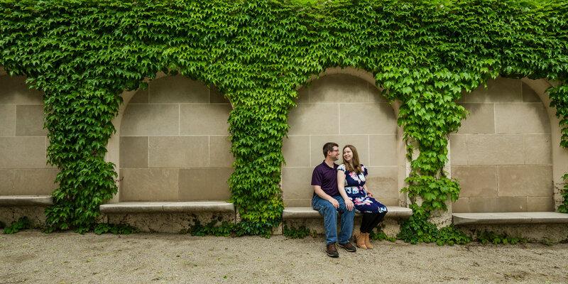 Couple sitting together under lush ivy arches, sharing a romantic moment during their engagement session at Longwood Gardens.