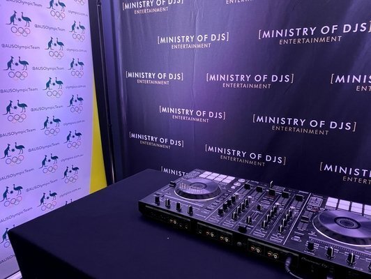 DJ equipment setup placed in front of branded backdrops for Ministry of DJs and Australian Olympic Team