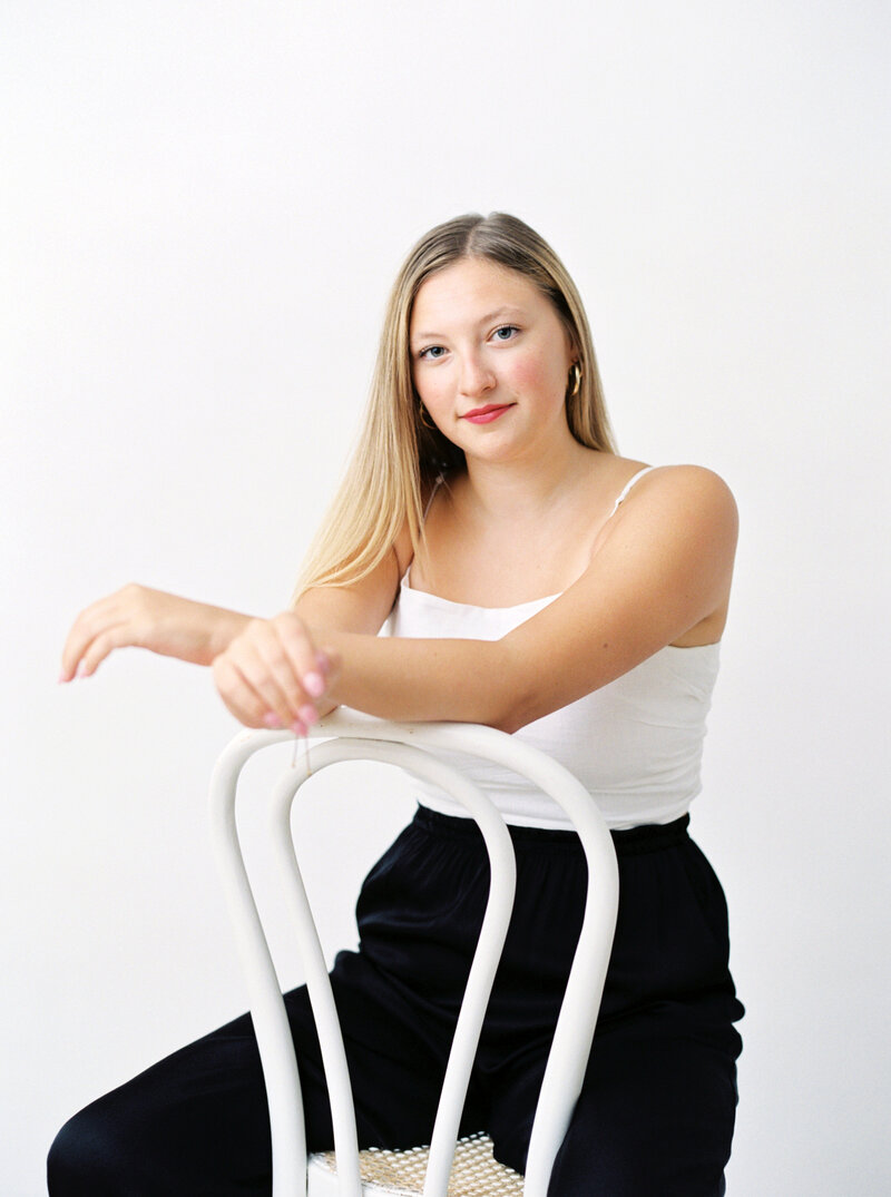 Woman in white top and black pants sits on backwards white chair