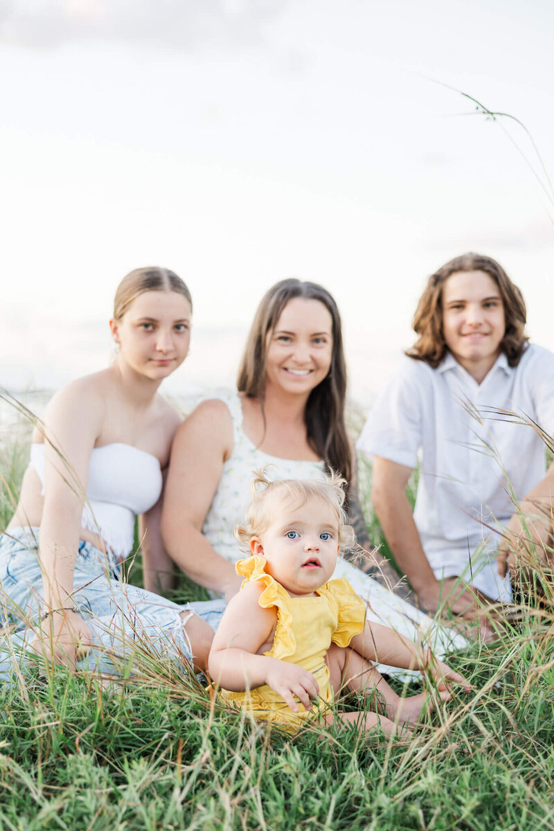 Mum with her three children, one of them being a toddler girl who is seated at the foreground, dressed in daffodil yellow.