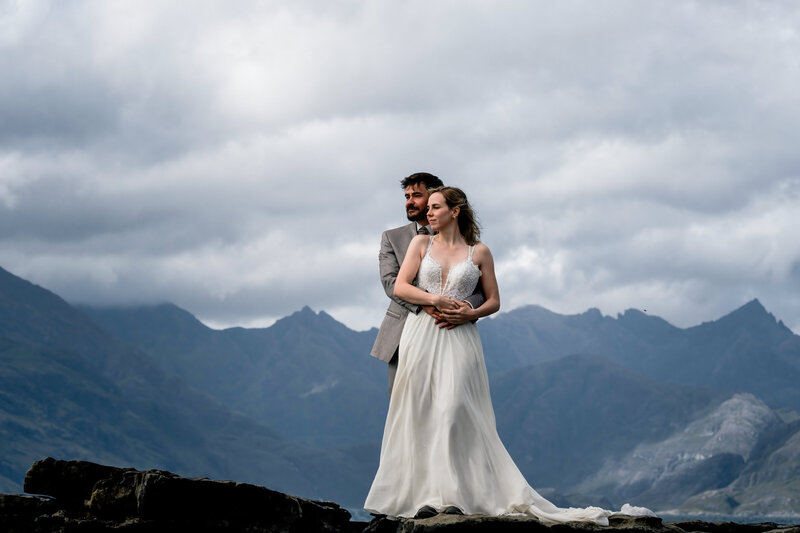 Bride and groom stand on rock with mountains behind them on skye during scottish elopement