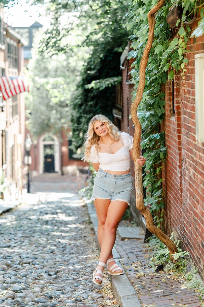 teen girl with blonde hair standing on a cobblestone street in boston wearing jean shorts and a white shirt