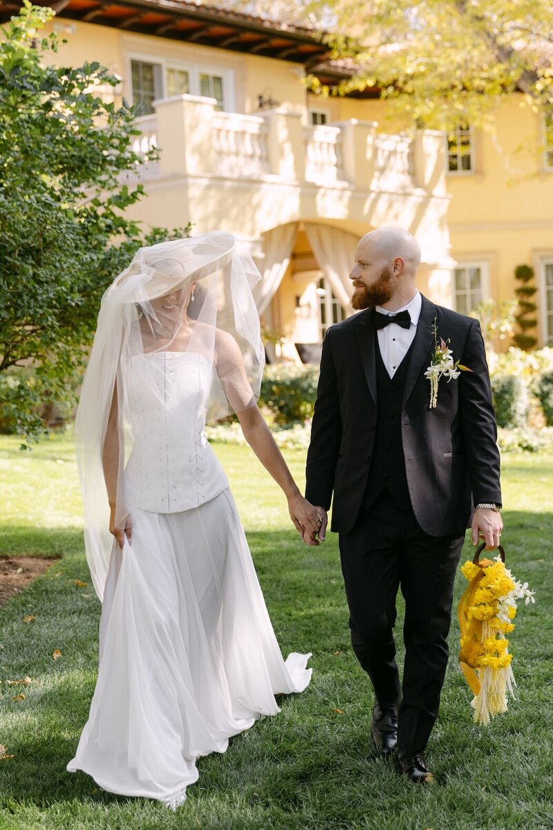 Bride and groom walking hand in hand on the lawn at Oceana's Gardens in Colorado, captured by a Colorado wedding photographer during their elegant outdoor celebration.