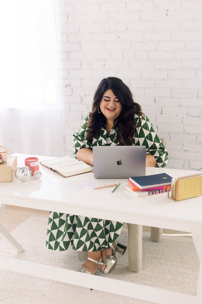 Marissa Martinez in a green and white patterned dress working at a white table with her laptop and Bible