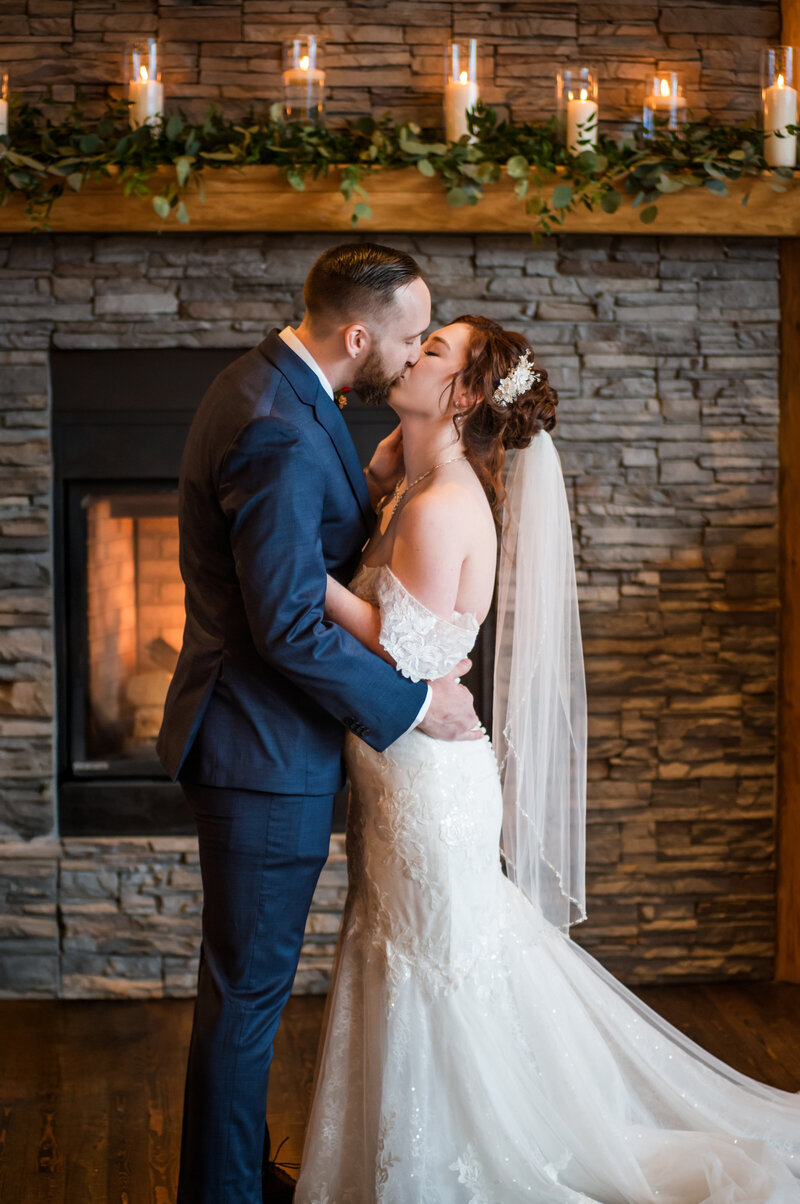 Wedding ceremony couple first kiss as newly weds. Big fireplace and candles in the back round at Fraser River Lodge Venue.