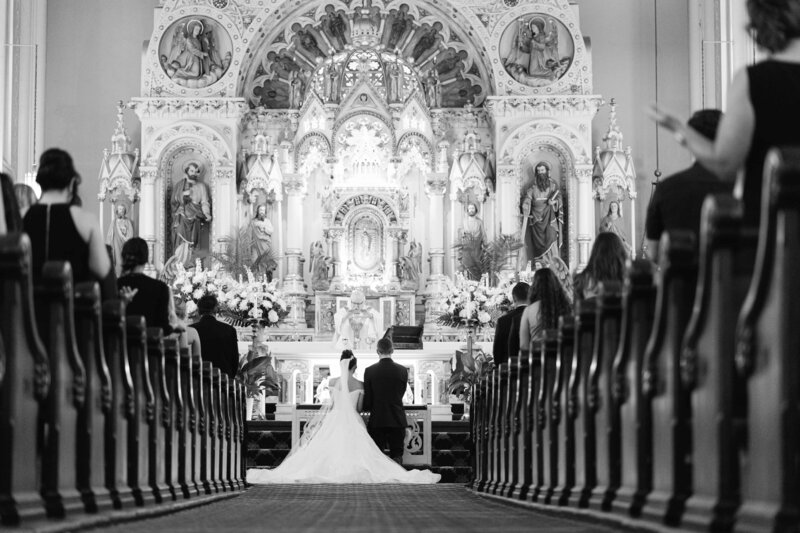 Black and white wedding portrait of bride and groom at alter in church.