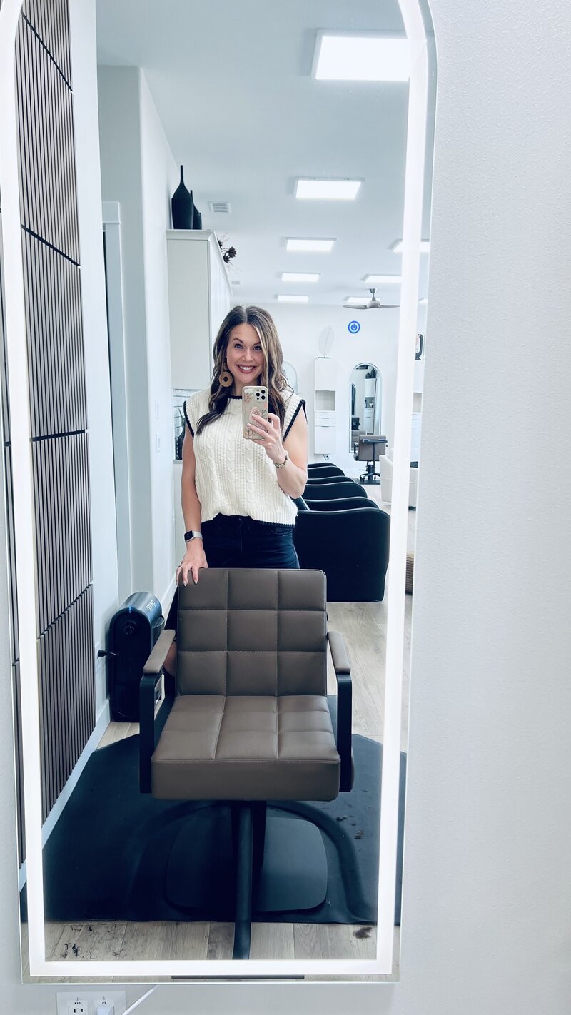 Modern salon styling stations at Tailored + Co featuring sleek neutral-toned cabinetry, arched mirrors, and plush styling chairs in a clean, luxurious setting. Designed to reflect high-end sophistication and comfort.