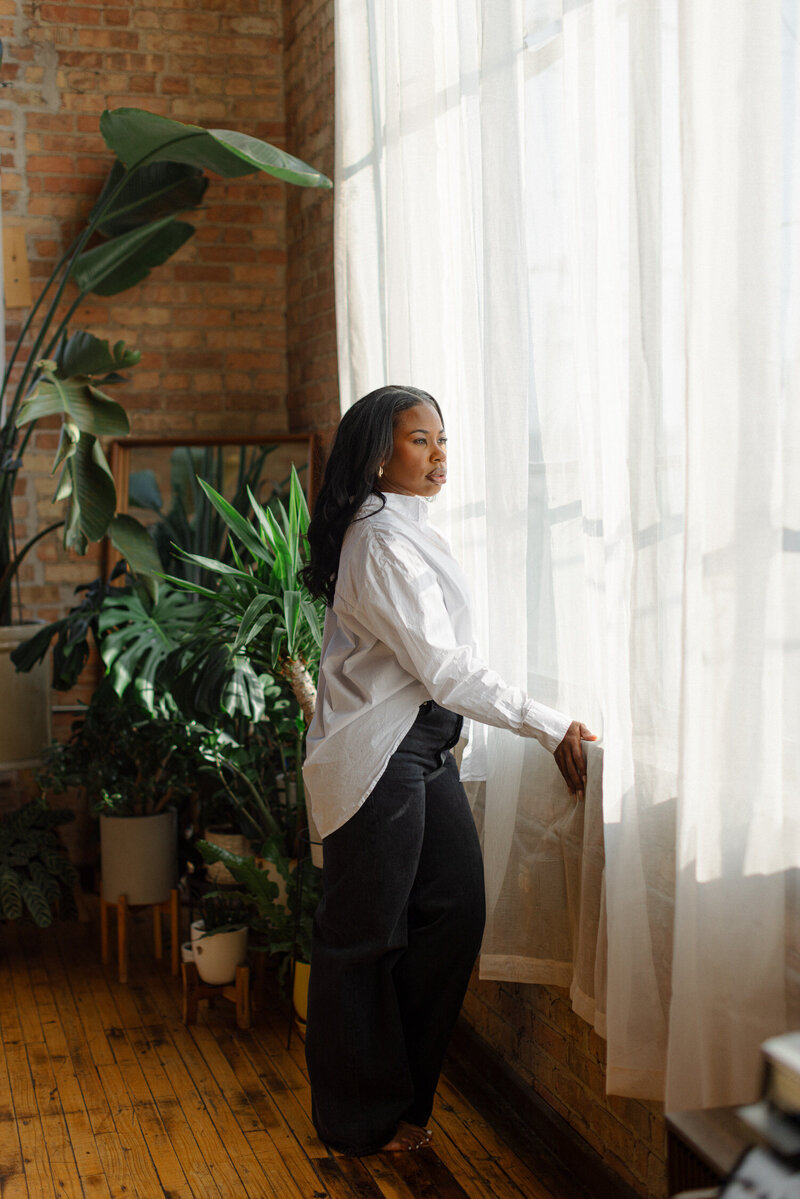 woman looking out of large window wearing a white shirt and jeans