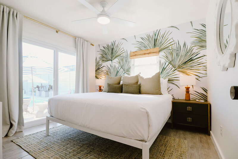 king bed with white linens green pillos and palm wallpaper