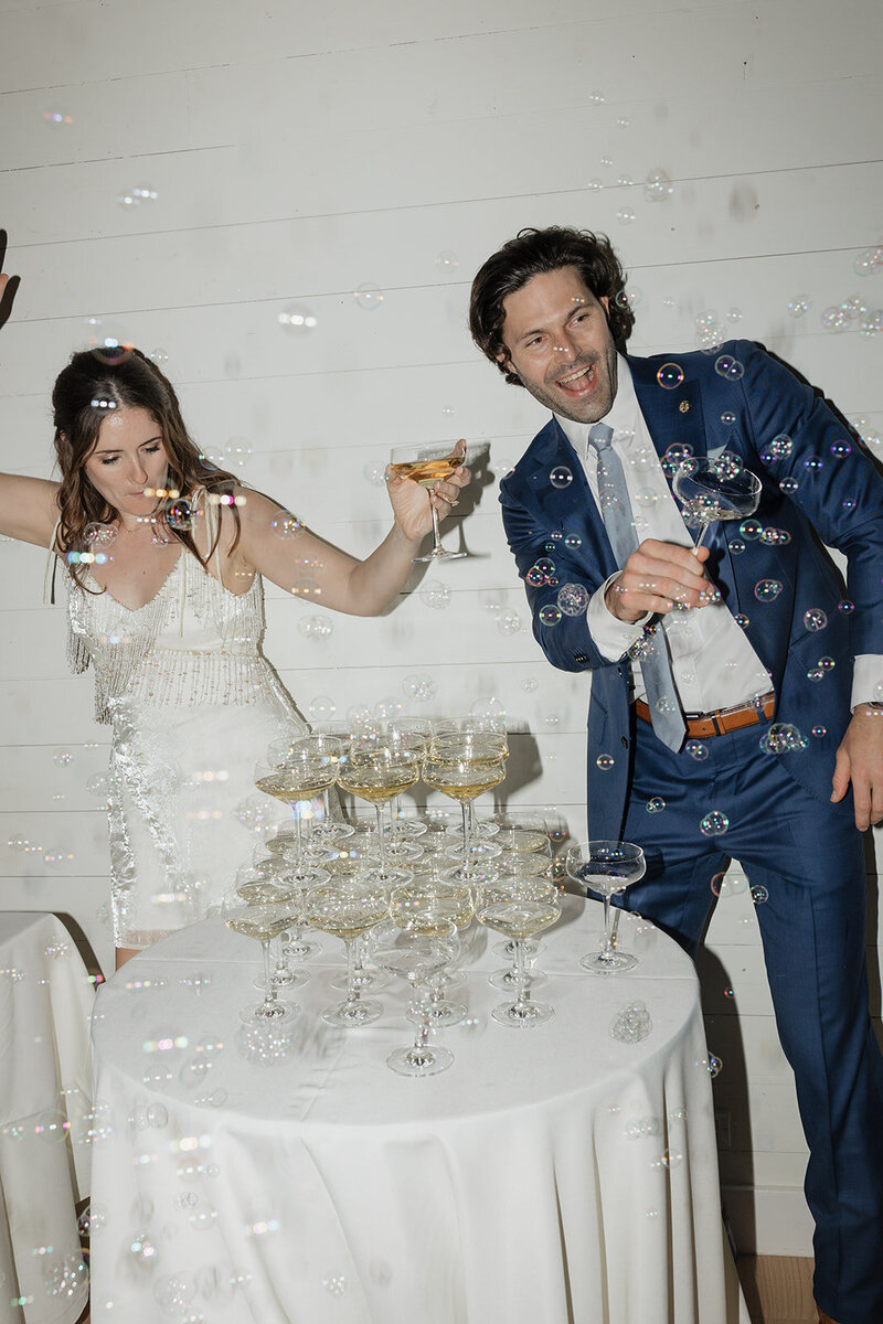 Bride and groom dancing with bubbles with champagne glasses in their hand.
