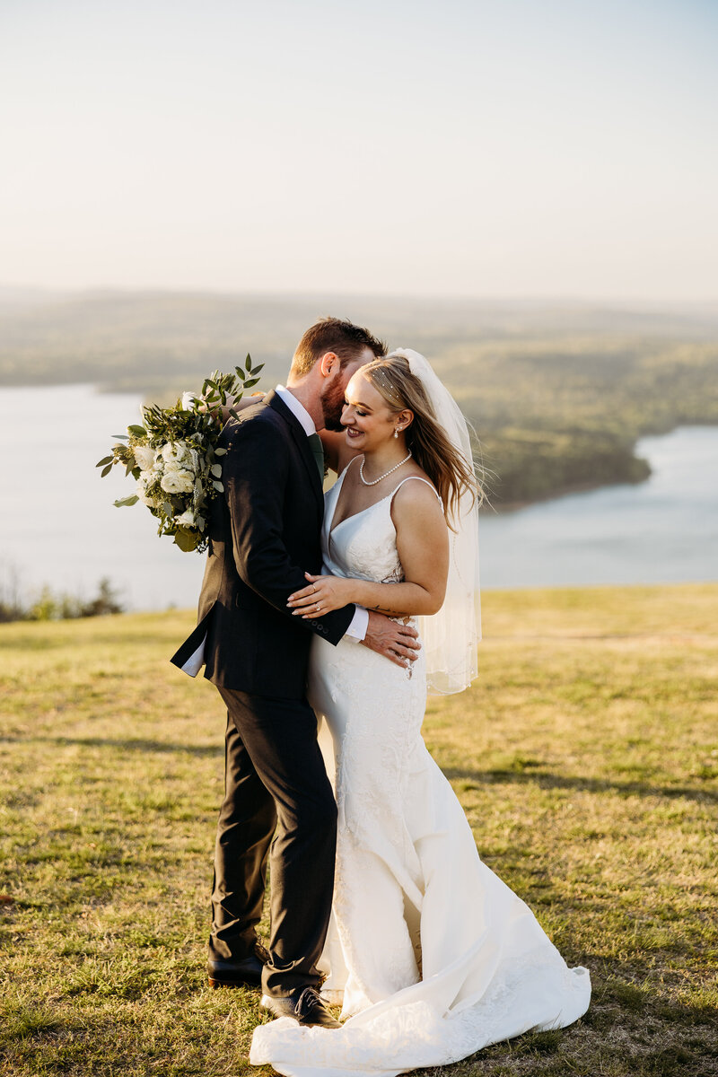 the bride and groom are facing each other and embracing while the groom whispers a silly joke into the brides ear to make her giggle