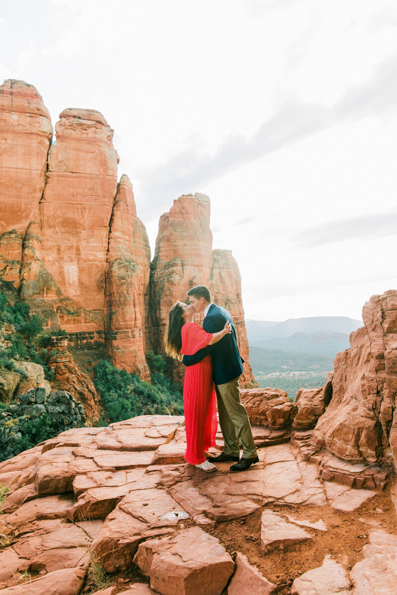 Romantic engagement photo of a couple kissing at the edge of a cliff in Sedona at Cathedral Rock