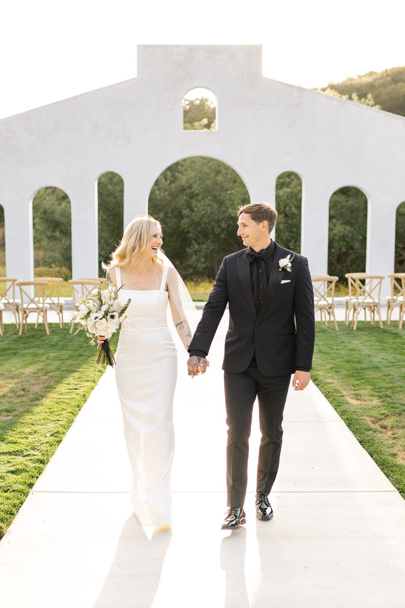 A newlywed bride and groom smiling and walking down the aisle at the stunning Juene Perché wedding Estate in Fallbrook